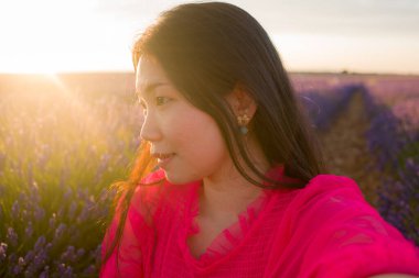 Yazlık elbiseli genç ve güzel Asyalı kadın romantik ve güzel mor lavanta çiçekleriyle eğleniyor doğa güzelliği kavramında.