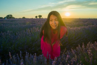 Genç ve güzel Asyalı yaz elbiseli kadın romantik güzellik ve özgürlük konseptiyle gün batımında mor lavanta çiçekleri tarlasında özgürce eğleniyor.