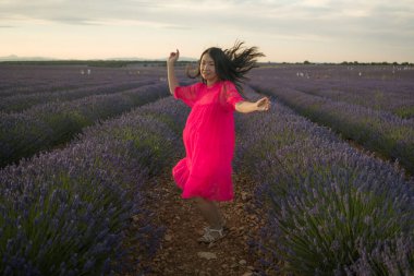 Genç, mutlu ve güzel yaz elbiseli Asyalı kadın doğanın tadını çıkarıyor. Açık havada, mor lavanta çiçeklerinin olduğu yerde romantik güzellik ve özgürlük kavramında.