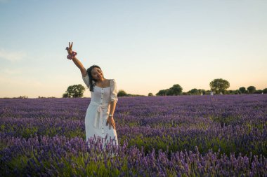 Açık havada, beyaz yaz elbiseli, mutlu ve çekici bir kadının romantik portresi seyahat ve tatil konseptindeki lavanta çiçekleri tarlasında tasasız eğleniyor.