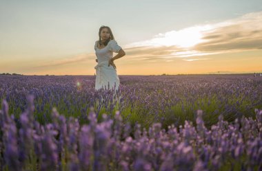 Açık havada, beyaz yaz elbiseli, mutlu ve çekici bir kadının romantik portresi seyahat ve tatil konseptindeki lavanta çiçekleri tarlasında tasasız eğleniyor.