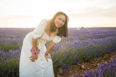 Açık havada, beyaz yaz elbiseli, mutlu ve çekici bir kadının romantik portresi seyahat ve tatil konseptindeki lavanta çiçekleri tarlasında tasasız eğleniyor.