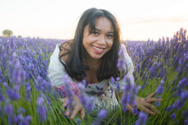 Açık havada, beyaz yaz elbiseli, mutlu ve çekici bir kadının romantik portresi seyahat ve tatil konseptindeki lavanta çiçekleri tarlasında tasasız eğleniyor.