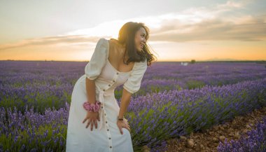 Açık havada, beyaz yaz elbiseli, mutlu ve çekici bir kadının romantik portresi seyahat ve tatil konseptindeki lavanta çiçekleri tarlasında tasasız eğleniyor.
