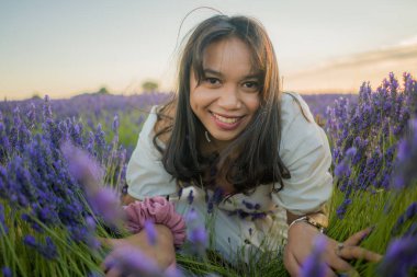 Açık havada, beyaz yaz elbiseli, mutlu ve çekici bir kadının romantik portresi seyahat ve tatil konseptindeki lavanta çiçekleri tarlasında tasasız eğleniyor.