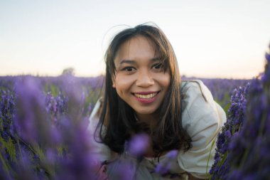 Açık havada, beyaz yaz elbiseli, mutlu ve çekici bir kadının romantik portresi seyahat ve tatil konseptindeki lavanta çiçekleri tarlasında tasasız eğleniyor.