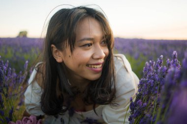 Açık havada, beyaz yaz elbiseli, mutlu ve çekici bir kadının romantik portresi seyahat ve tatil konseptindeki lavanta çiçekleri tarlasında tasasız eğleniyor.