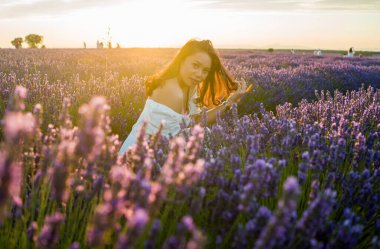 Açık havada, beyaz yaz elbiseli, mutlu ve çekici bir kadının romantik portresi seyahat ve tatil konseptindeki lavanta çiçekleri tarlasında tasasız eğleniyor.