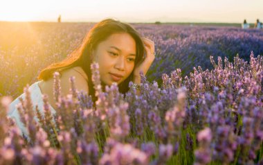 Açık havada, beyaz yaz elbiseli, mutlu ve çekici bir kadının romantik portresi seyahat ve tatil konseptindeki lavanta çiçekleri tarlasında tasasız eğleniyor.