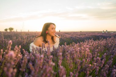 Açık havada, beyaz yaz elbiseli, mutlu ve çekici bir kadının romantik portresi seyahat ve tatil konseptindeki lavanta çiçekleri tarlasında tasasız eğleniyor.