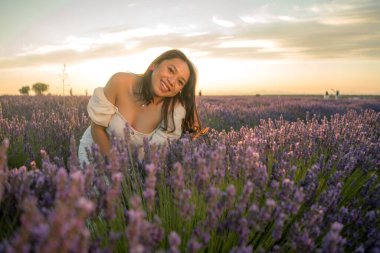 Açık havada, beyaz yaz elbiseli, mutlu ve çekici bir kadının romantik portresi seyahat ve tatil konseptindeki lavanta çiçekleri tarlasında tasasız eğleniyor.