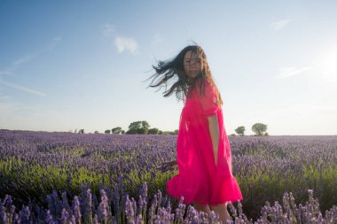 Genç Asyalı kadın lavanta çiçekleri tarlasında mutlu ve güzel bir Çinli kız tatlı mavi elbisesiyle tatilin tadını çıkarıyor mor çiçekli çayırlarda dinleniyor.