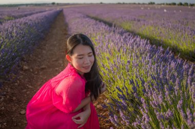 Genç Asyalı kadın lavanta çiçekleri tarlasında mutlu ve güzel bir Çinli kız tatlı mavi elbisesiyle tatilin tadını çıkarıyor mor çiçekli çayırlarda dinleniyor.