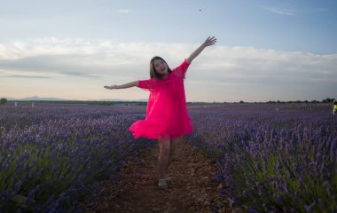 Genç Asyalı kadın lavanta çiçekleri tarlasında mutlu ve güzel bir Çinli kız tatlı mavi elbisesiyle tatilin tadını çıkarıyor mor çiçekli çayırlarda dinleniyor.