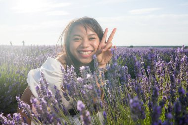 Açık havada, beyaz yaz elbiseli, mutlu ve çekici bir kadının romantik portresi seyahat ve tatil konseptindeki lavanta çiçekleri tarlasında tasasız eğleniyor.