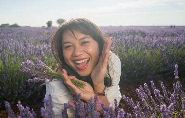 Açık havada, beyaz yaz elbiseli, mutlu ve çekici bir kadının romantik portresi seyahat ve tatil konseptindeki lavanta çiçekleri tarlasında tasasız eğleniyor.