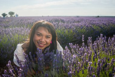 Açık havada, beyaz yaz elbiseli, mutlu ve çekici bir kadının romantik portresi seyahat ve tatil konseptindeki lavanta çiçekleri tarlasında tasasız eğleniyor.