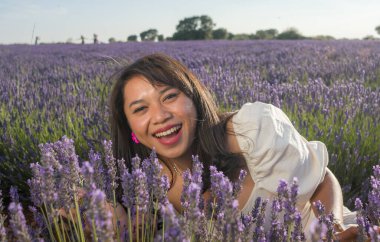 Açık havada, beyaz yaz elbiseli, mutlu ve çekici bir kadının romantik portresi seyahat ve tatil konseptindeki lavanta çiçekleri tarlasında tasasız eğleniyor.