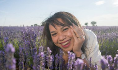 Açık havada, beyaz yaz elbiseli, mutlu ve çekici bir kadının romantik portresi seyahat ve tatil konseptindeki lavanta çiçekleri tarlasında tasasız eğleniyor.