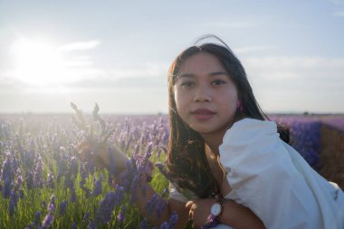 Açık havada, beyaz yaz elbiseli, mutlu ve çekici bir kadının romantik portresi seyahat ve tatil konseptindeki lavanta çiçekleri tarlasında tasasız eğleniyor.