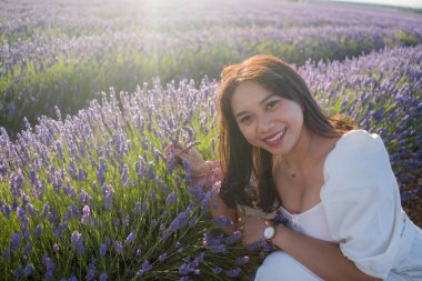 Açık havada, beyaz yaz elbiseli, mutlu ve çekici bir kadının romantik portresi seyahat ve tatil konseptindeki lavanta çiçekleri tarlasında tasasız eğleniyor.
