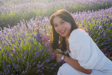 Açık havada, beyaz yaz elbiseli, mutlu ve çekici bir kadının romantik portresi seyahat ve tatil konseptindeki lavanta çiçekleri tarlasında tasasız eğleniyor.