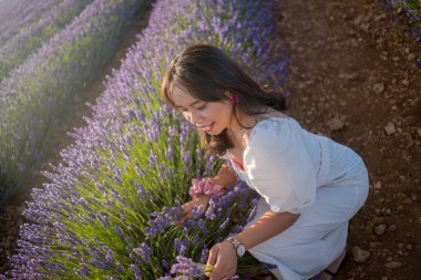 Açık havada, beyaz yaz elbiseli, mutlu ve çekici bir kadının romantik portresi seyahat ve tatil konseptindeki lavanta çiçekleri tarlasında tasasız eğleniyor.