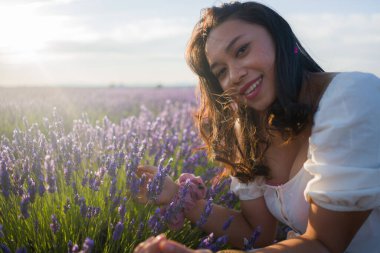 Açık havada, beyaz yaz elbiseli, mutlu ve çekici bir kadının romantik portresi seyahat ve tatil konseptindeki lavanta çiçekleri tarlasında tasasız eğleniyor.