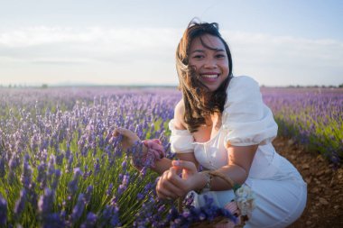 Açık havada, beyaz yaz elbiseli, mutlu ve çekici bir kadının romantik portresi seyahat ve tatil konseptindeki lavanta çiçekleri tarlasında tasasız eğleniyor.