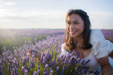 Açık havada, beyaz yaz elbiseli, mutlu ve çekici bir kadının romantik portresi seyahat ve tatil konseptindeki lavanta çiçekleri tarlasında tasasız eğleniyor.