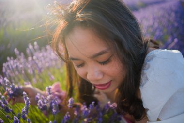 Açık havada, beyaz yaz elbiseli, mutlu ve çekici bir kadının romantik portresi seyahat ve tatil konseptindeki lavanta çiçekleri tarlasında tasasız eğleniyor.