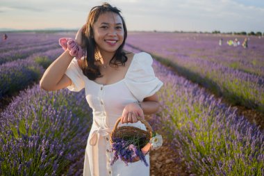 Açık havada, beyaz yaz elbiseli, mutlu ve çekici bir kadının romantik portresi seyahat ve tatil konseptindeki lavanta çiçekleri tarlasında tasasız eğleniyor.