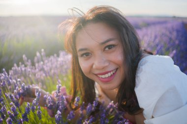 Açık havada, beyaz yaz elbiseli, mutlu ve çekici bir kadının romantik portresi seyahat ve tatil konseptindeki lavanta çiçekleri tarlasında tasasız eğleniyor.