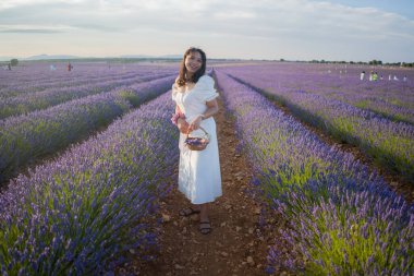 Açık havada, beyaz yaz elbiseli, mutlu ve çekici bir kadının romantik portresi seyahat ve tatil konseptindeki lavanta çiçekleri tarlasında tasasız eğleniyor.