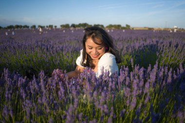 Açık havada, beyaz yaz elbiseli, mutlu ve çekici bir kadının romantik portresi seyahat ve tatil konseptindeki lavanta çiçekleri tarlasında tasasız eğleniyor.