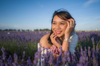 Açık havada, beyaz yaz elbiseli, mutlu ve çekici bir kadının romantik portresi seyahat ve tatil konseptindeki lavanta çiçekleri tarlasında tasasız eğleniyor.