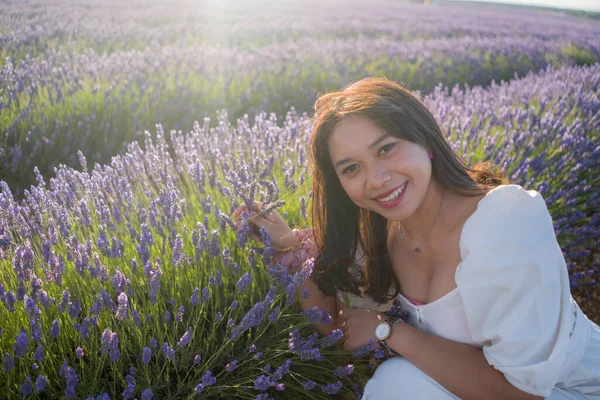 Açık havada, beyaz yaz elbiseli, mutlu ve çekici bir kadının romantik portresi seyahat ve tatil konseptindeki lavanta çiçekleri tarlasında tasasız eğleniyor.