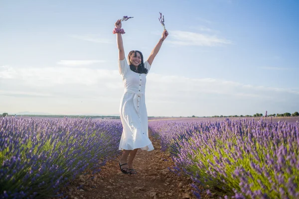 Açık havada, beyaz yaz elbiseli, mutlu ve çekici bir kadının romantik portresi seyahat ve tatil konseptindeki lavanta çiçekleri tarlasında tasasız eğleniyor.
