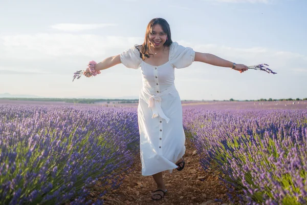 Açık havada, beyaz yaz elbiseli, mutlu ve çekici bir kadının romantik portresi seyahat ve tatil konseptindeki lavanta çiçekleri tarlasında tasasız eğleniyor.