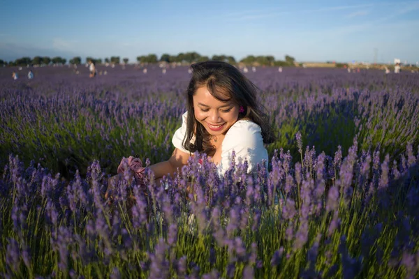 Açık havada, beyaz yaz elbiseli, mutlu ve çekici bir kadının romantik portresi seyahat ve tatil konseptindeki lavanta çiçekleri tarlasında tasasız eğleniyor.