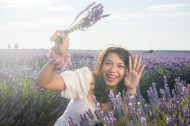 Açık havada, beyaz yaz elbiseli, mutlu ve çekici bir kadının romantik portresi seyahat ve tatil konseptindeki lavanta çiçekleri tarlasında tasasız eğleniyor.