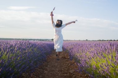 Açık havada, beyaz yaz elbiseli, mutlu ve çekici bir kadının romantik portresi seyahat ve tatil konseptindeki lavanta çiçekleri tarlasında tasasız eğleniyor.