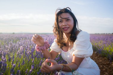 Açık havada, beyaz yaz elbiseli, mutlu ve çekici bir kadının romantik portresi seyahat ve tatil konseptindeki lavanta çiçekleri tarlasında tasasız eğleniyor.