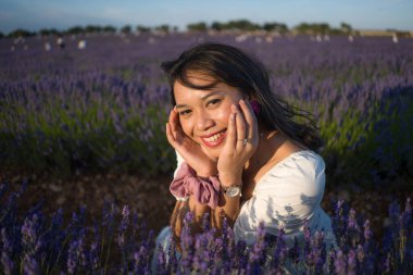 Açık havada, beyaz yaz elbiseli, mutlu ve çekici bir kadının romantik portresi seyahat ve tatil konseptindeki lavanta çiçekleri tarlasında tasasız eğleniyor.
