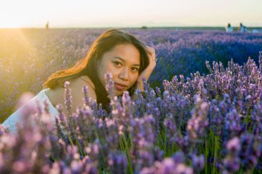 Açık havada, beyaz yaz elbiseli, mutlu ve çekici bir kadının romantik portresi seyahat ve tatil konseptindeki lavanta çiçekleri tarlasında tasasız eğleniyor.