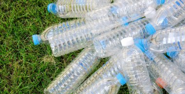 Arka planda çimen olan plastik şişelerden bir yığın..