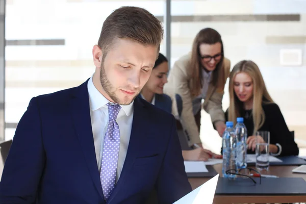 Heureux homme d'affaires intelligent avec des coéquipiers discutant en arrière-plan — Photo