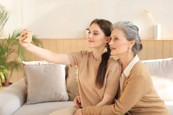 Happy middle aged mother and daughter taking selfie at home