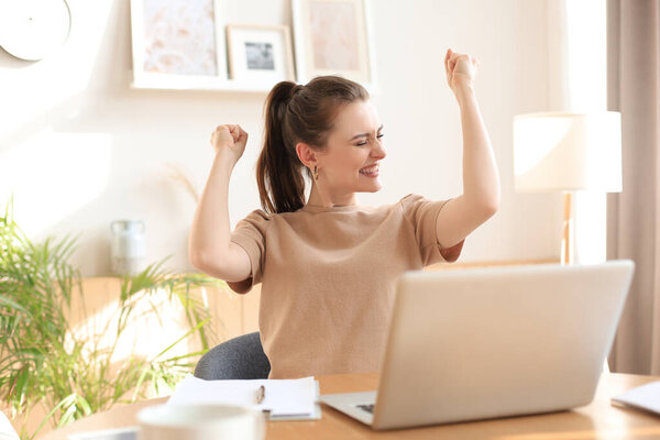 Happy entrepreneur woman sit at desk reading good news and express joy rising hands up