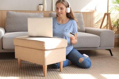 Oturma odasında kredi kartı ve laptop kullanan mutlu doğal sarışın..